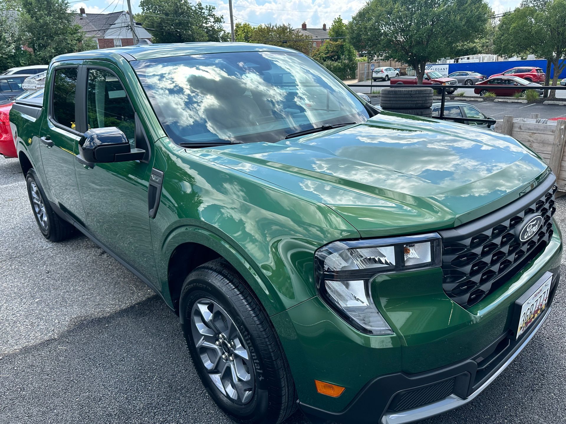 Green Ford Maverick truck parked outdoors, reflecting sky, sunny day.