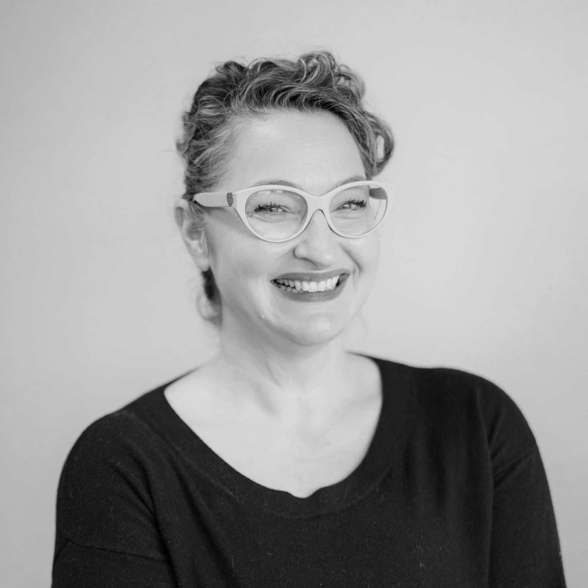 A woman wearing glasses and a black shirt is smiling in a black and white photo.