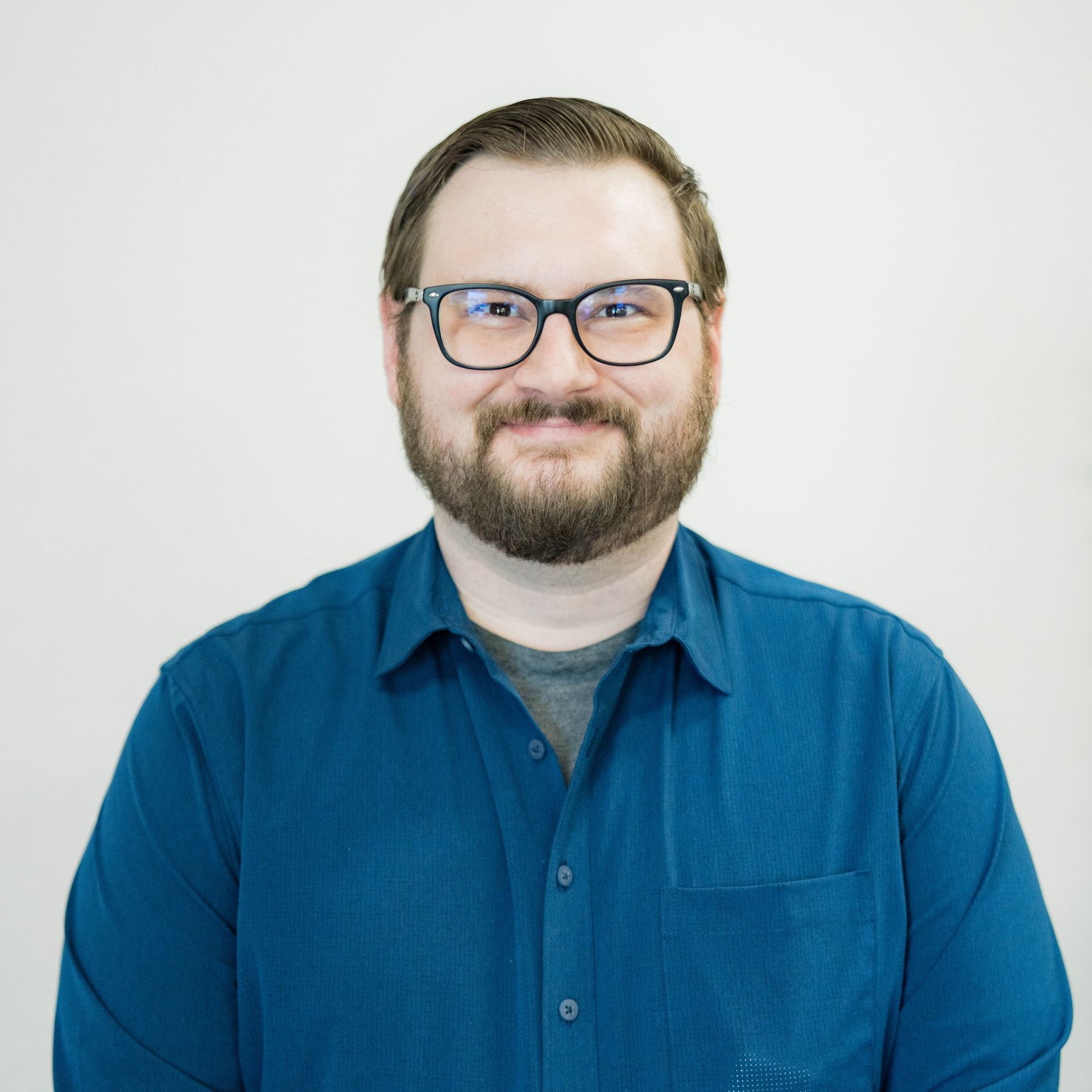 A man in a blue shirt is smiling with his arms crossed