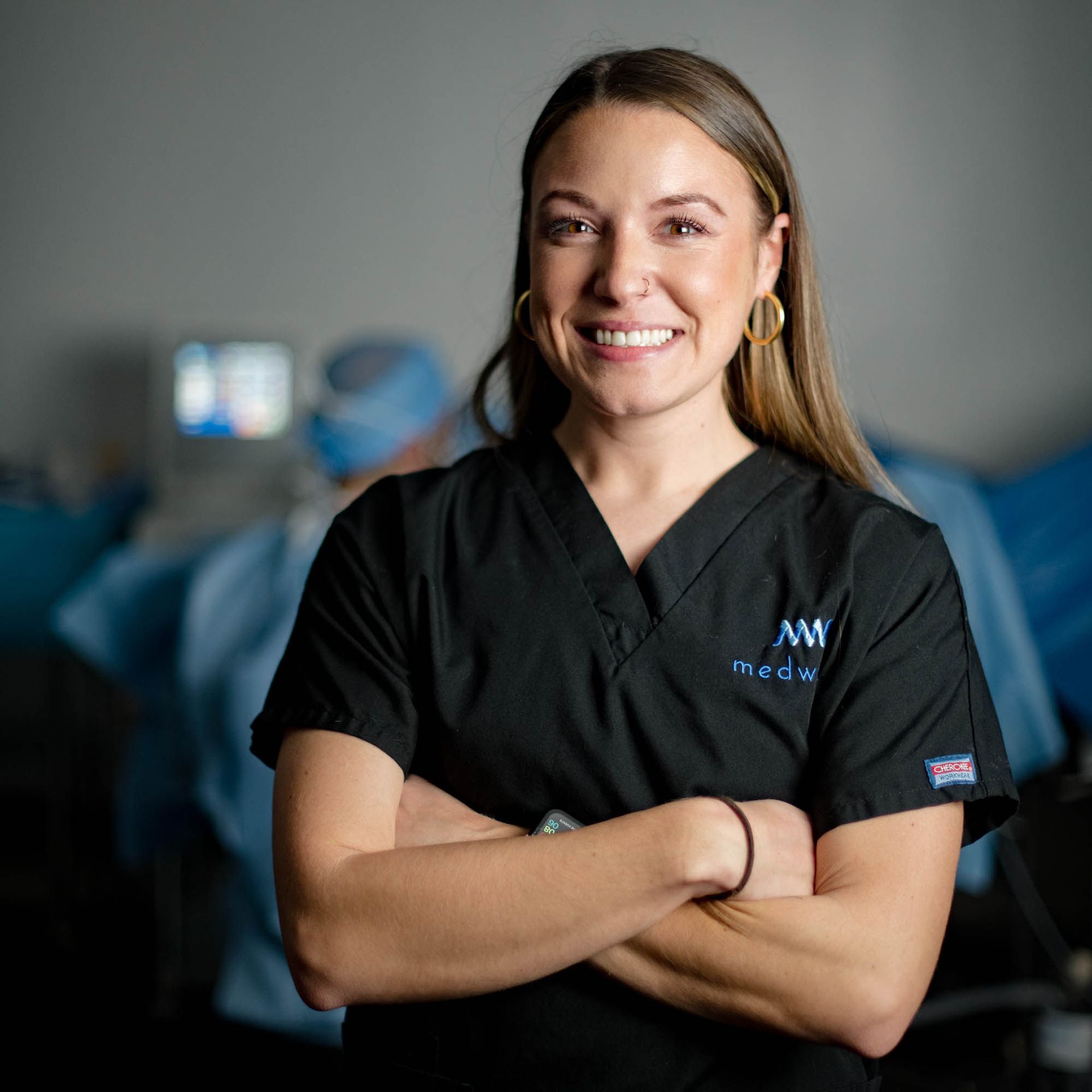 A woman in a black scrub is smiling with her arms crossed
