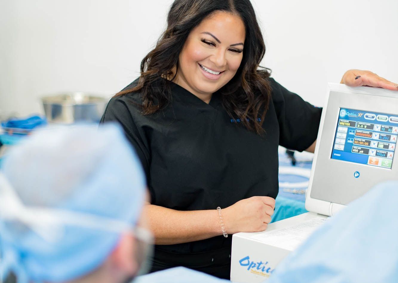 A woman is smiling while holding a tablet in an operating room.