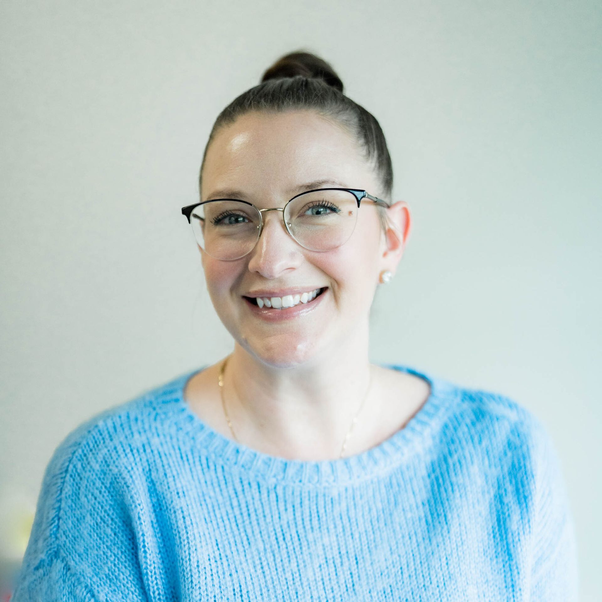A woman wearing glasses and a blue sweater is smiling for the camera.