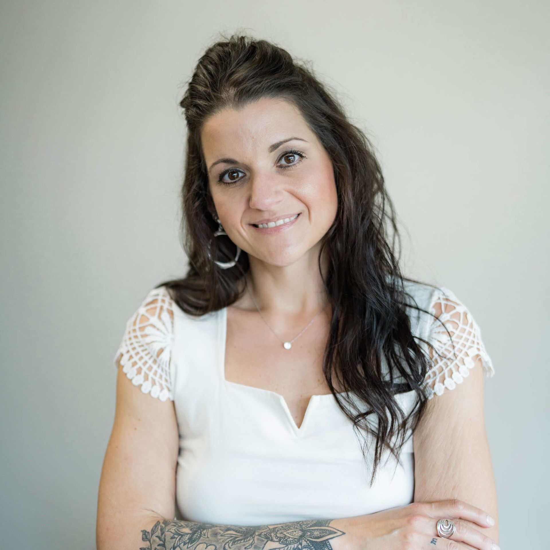 A woman with a tattoo on her arm is wearing a white shirt and smiling.