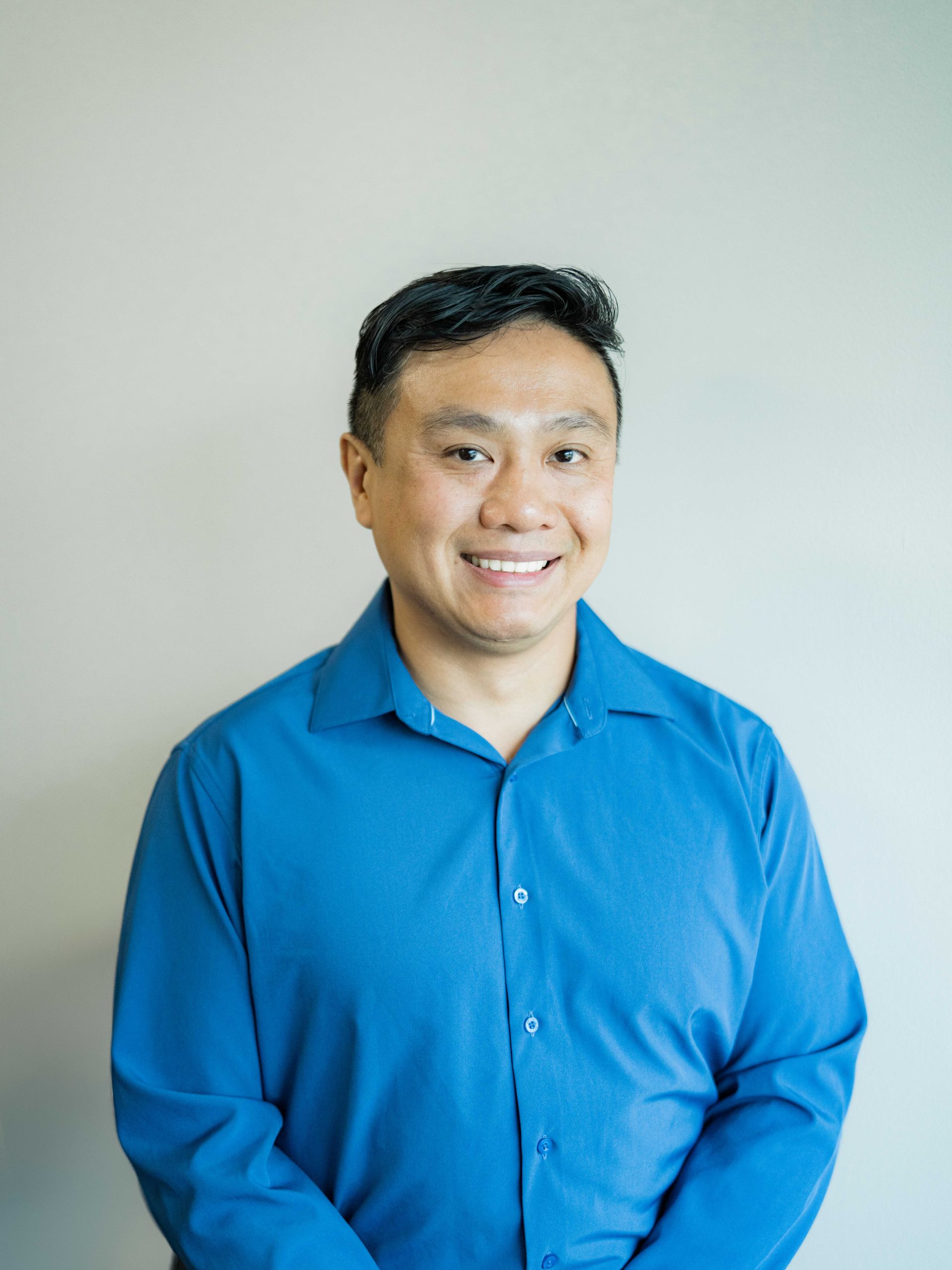 A man in a blue shirt is smiling with his arms crossed