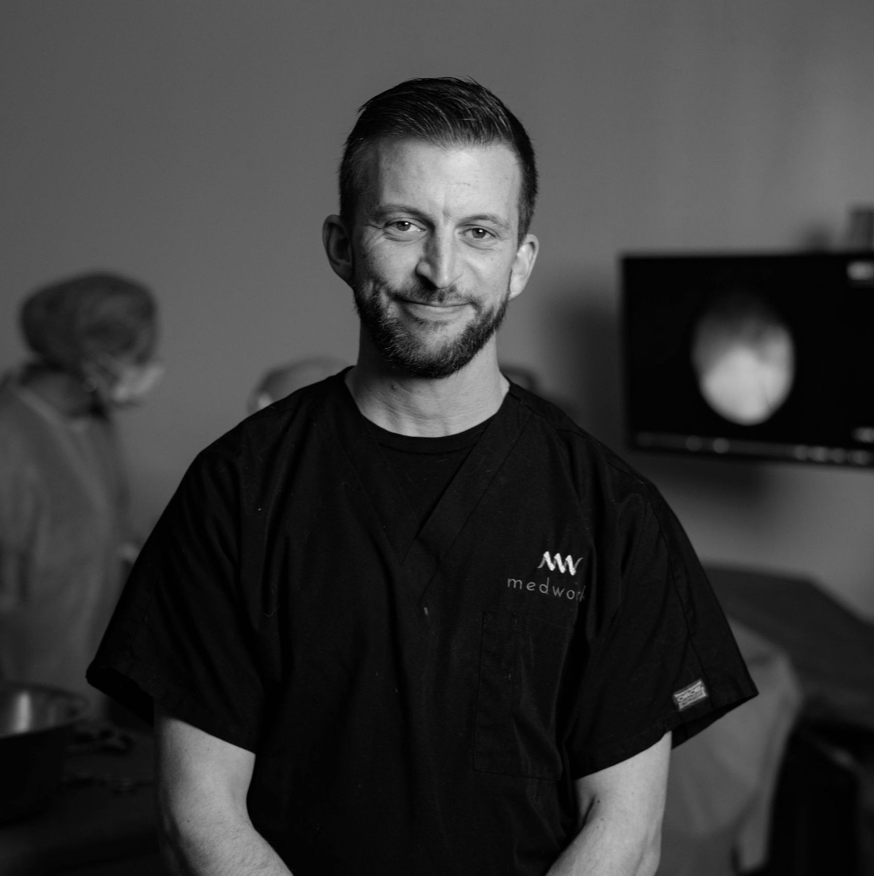 A man with a beard is wearing a black shirt with the letter m on it.