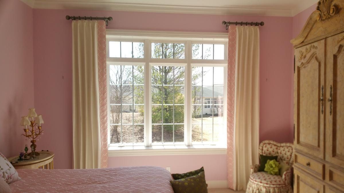 A bedroom with pink walls , a bed , a chair and a window.