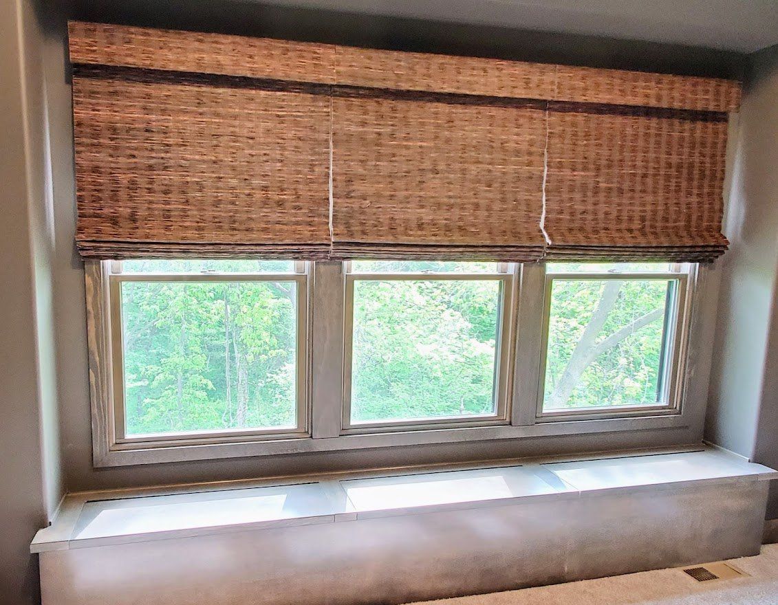 A room with three windows and a wicker blind on the window.