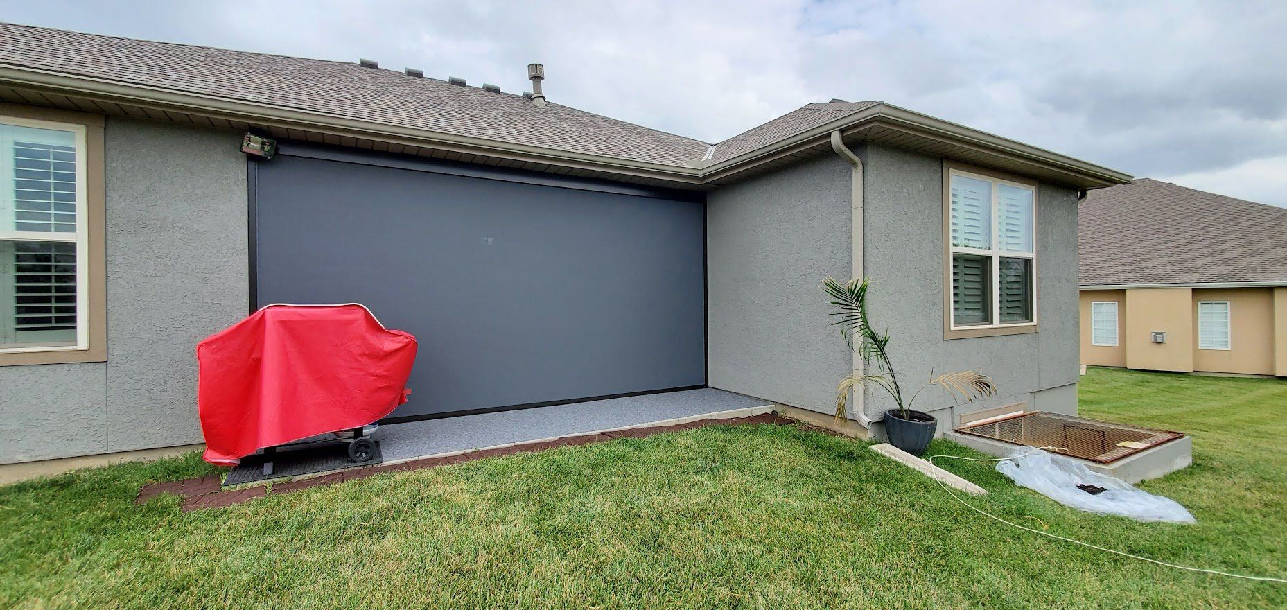 A red grill is sitting in front of a house with a garage door.