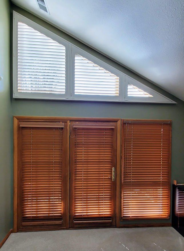 A room with a triangle shaped window and wooden blinds.