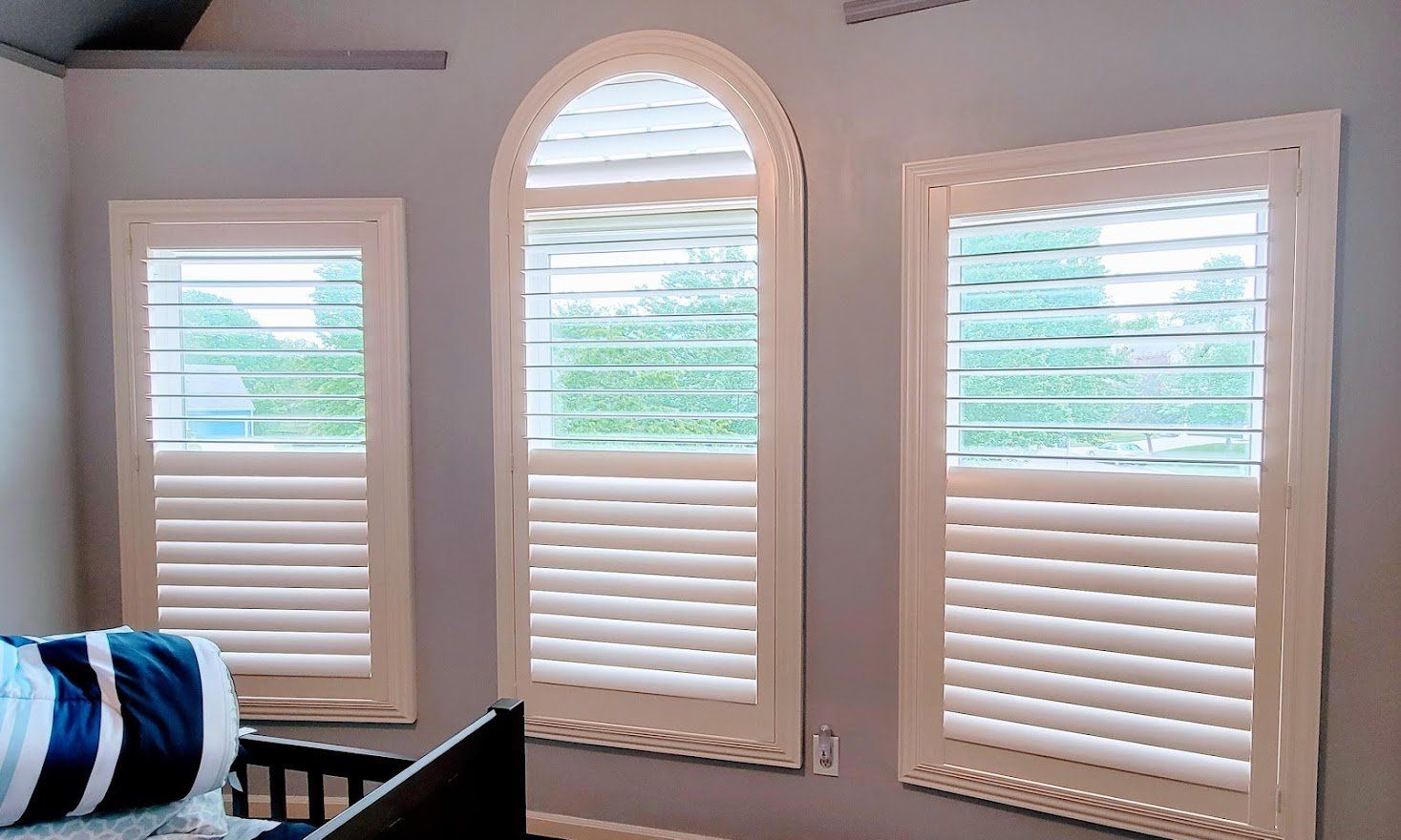 A bedroom with three arched windows and white shutters.