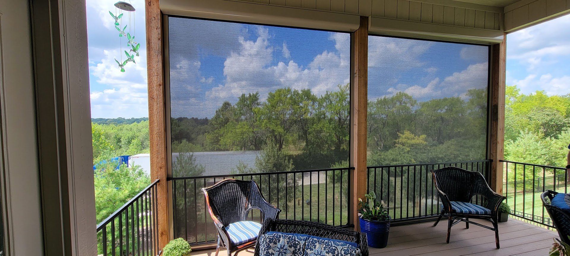 A screened in porch with a view of trees and a lake.