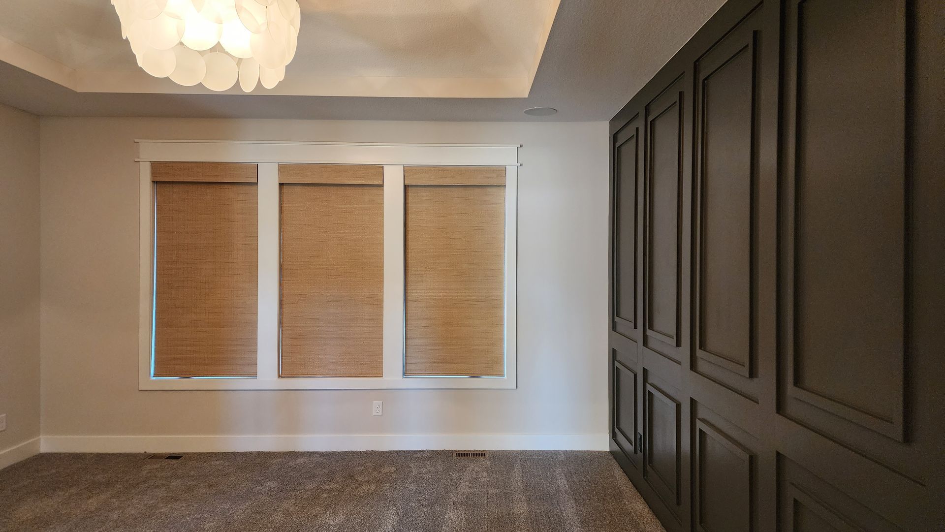 An empty room with three windows and a chandelier.