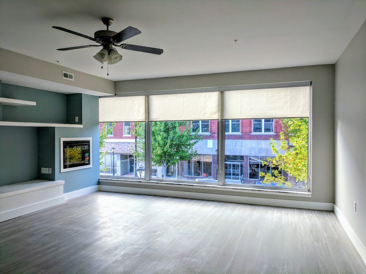An empty living room with a large window and a ceiling fan.