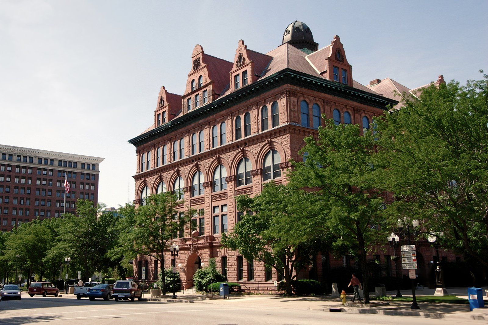 A large brick building is surrounded by trees and cars
