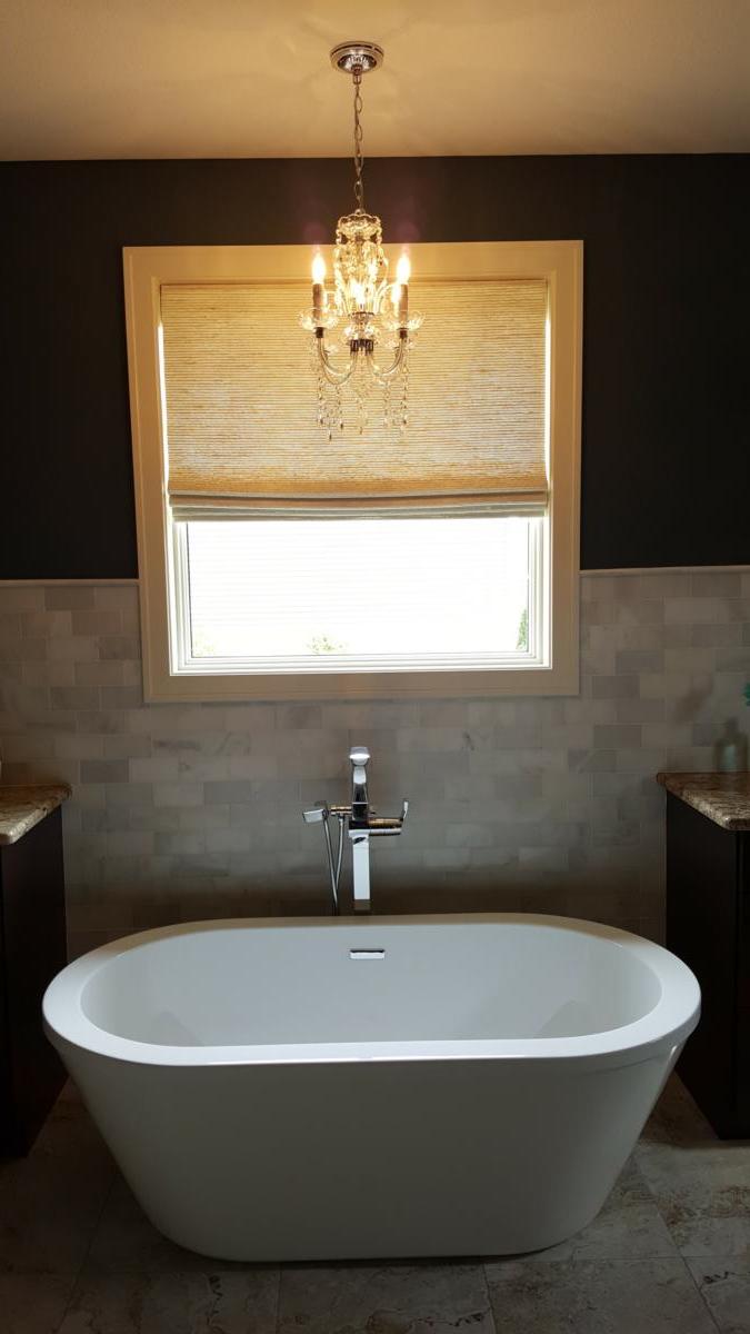A bathtub in a bathroom next to a window with a chandelier hanging from the ceiling.