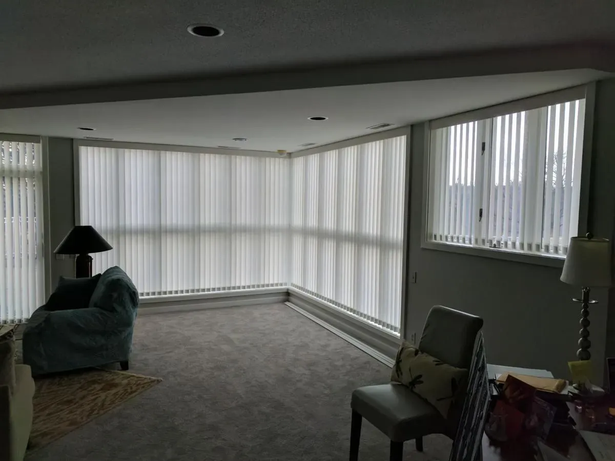 A living room with a lot of windows and vertical blinds.