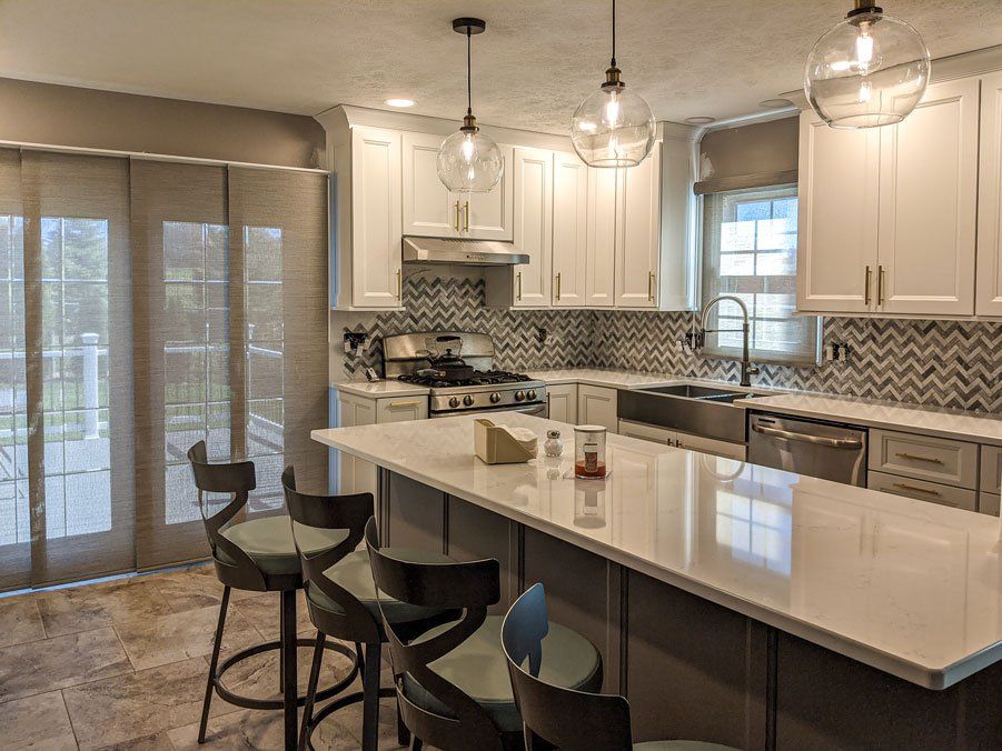 A kitchen with white cabinets , a large island , stools and a stove.