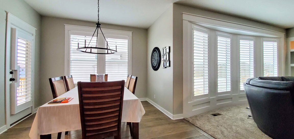 A dining room with a table and chairs and shutters on the windows.