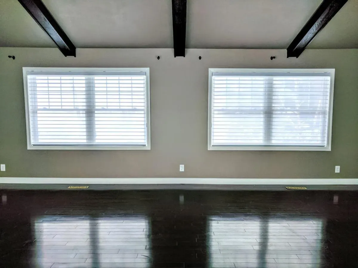 An empty living room with two windows and a wooden floor.