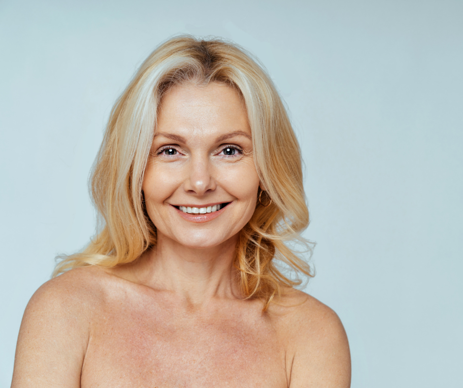 A smiling person with shoulder-length blonde hair and bare shoulders against a light blue background.