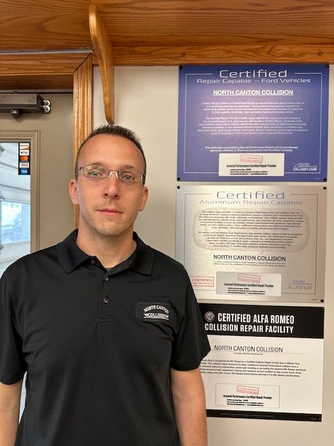 A man in a black shirt is standing in front of a wall with certified signs on it.