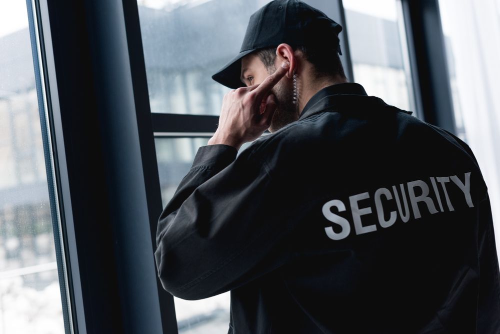 A Security Guard is Looking Out of a Window and Talking on a Cell Phone — Asset Security Group In Taree, NSW