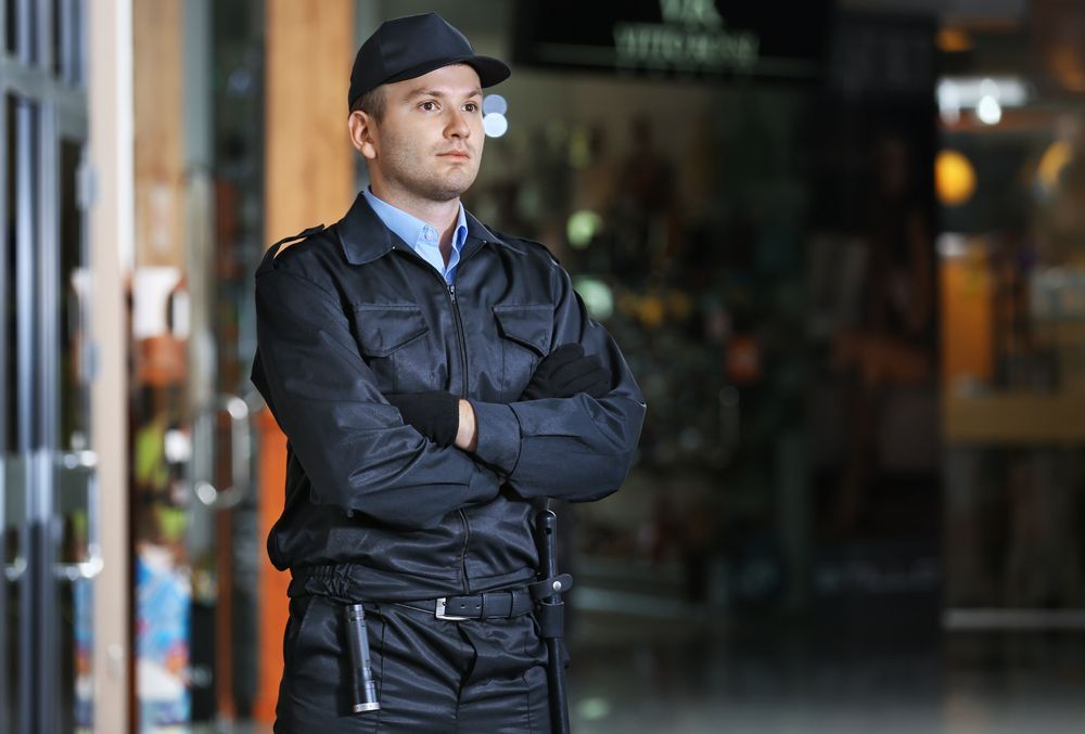 A Security Guard Is Standing With His Arms Crossed In Front Of A Door — Asset Security Group In Coffs Harbour, NSW