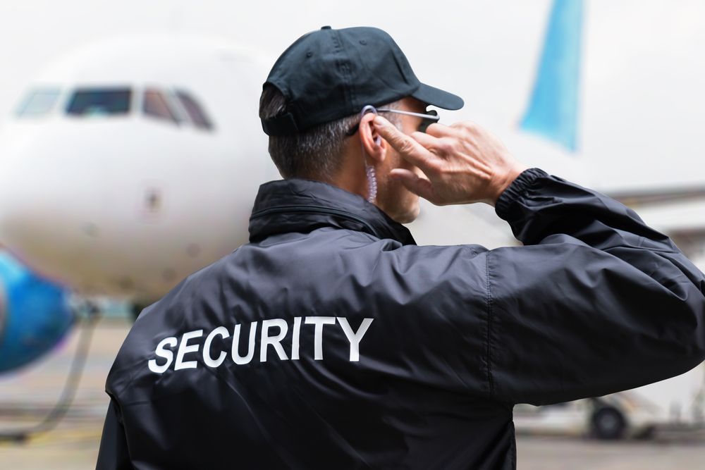 A Security Guard is Talking on a Cell Phone in Front of an Airplane — Asset Security Group In Newcastle, NSW