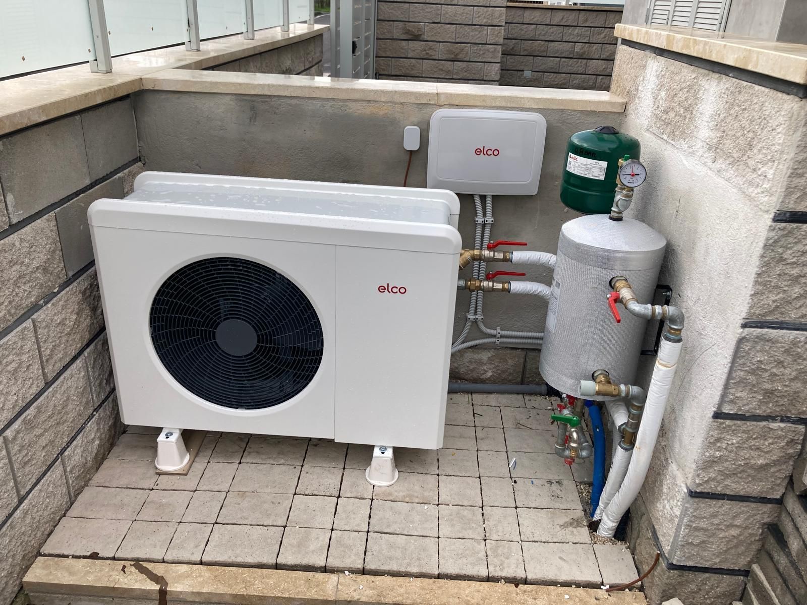 Un condizionatore bianco è appoggiato su un pavimento piastrellato, accanto a un muro di mattoni.