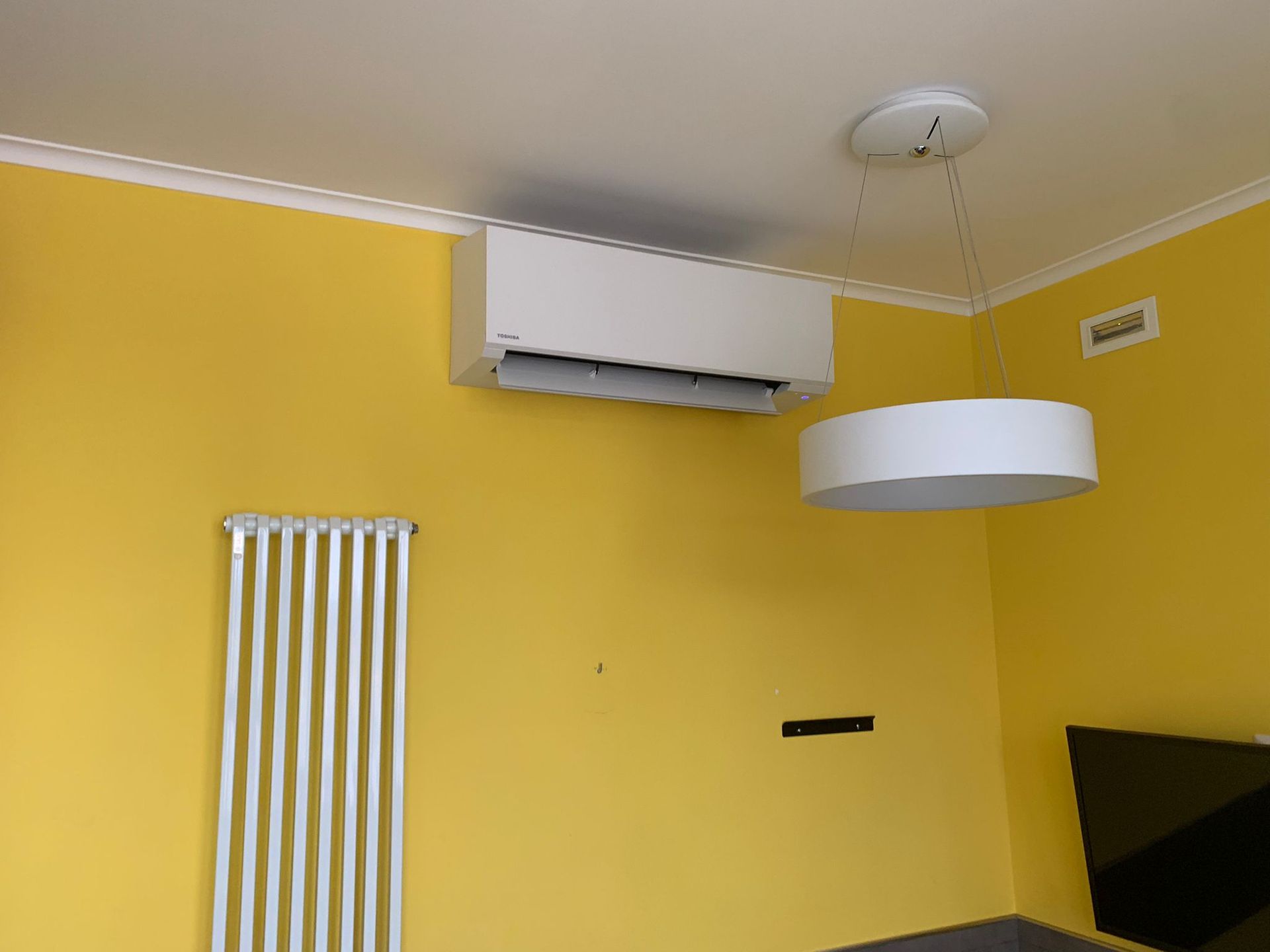 Un soggiorno con pareti gialle e un condizionatore bianco appeso al soffitto.