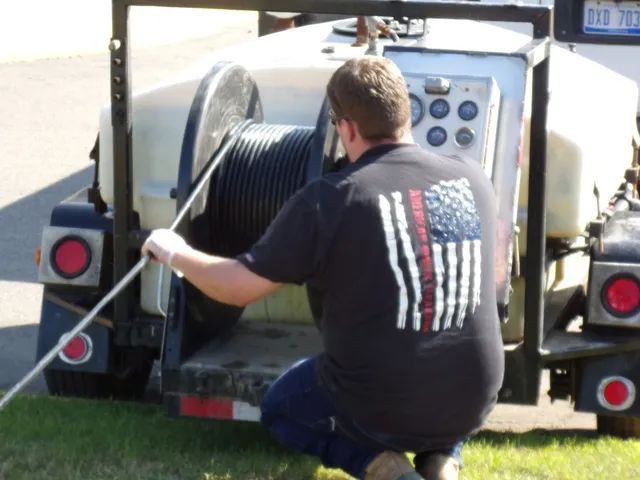 Man in a black shirt with American flag graphic, working with a large cable reel on a trailer.