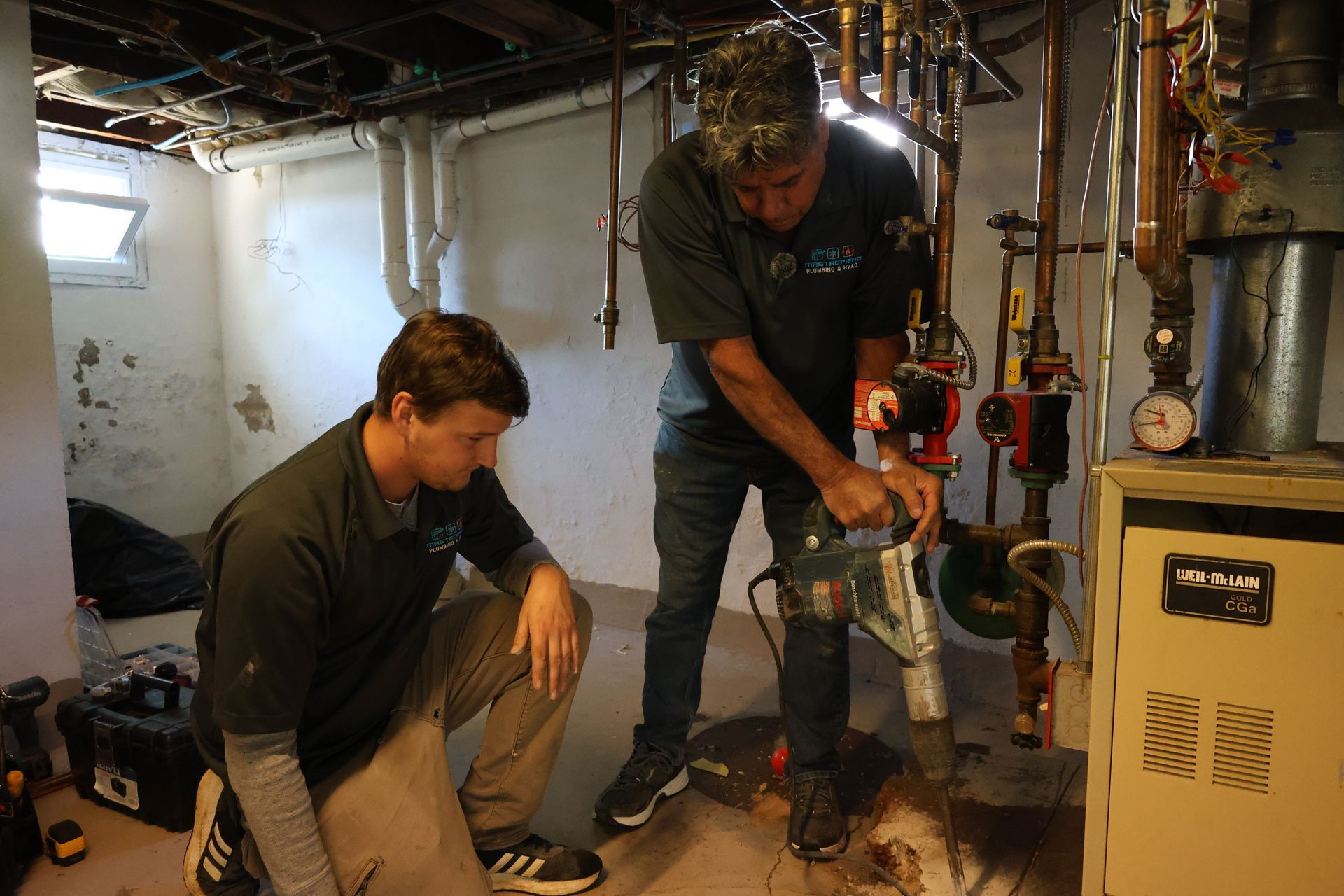 Two men are working on a heating system in a basement.