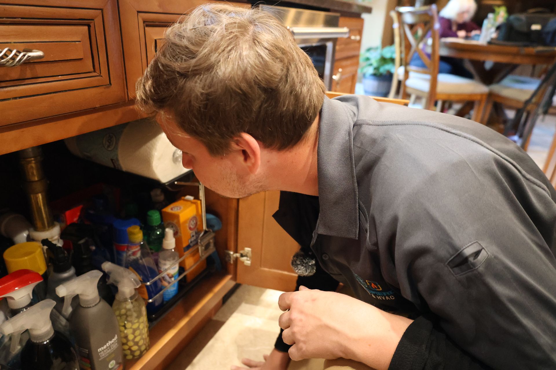 A man is looking under a sink in a kitchen.