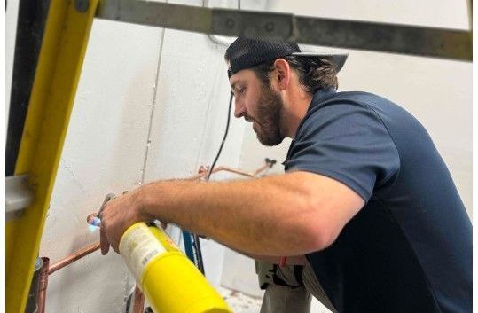 A man is working on a pipe with a ladder.