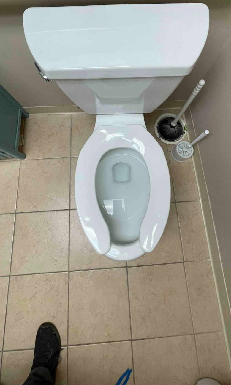 A person is standing next to a toilet in a bathroom.