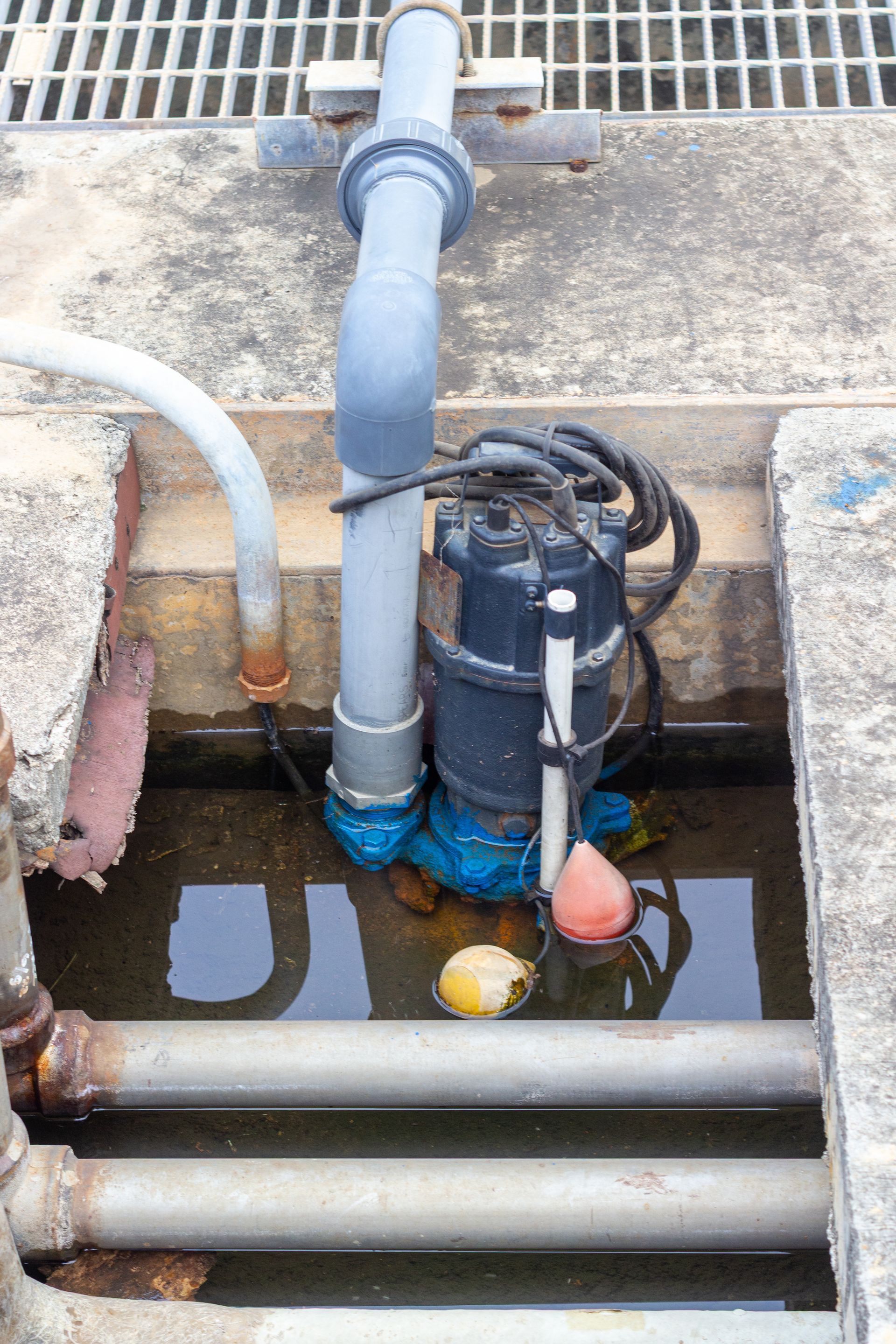 Submersible pump in a concrete pit with water, pipes, and a float.