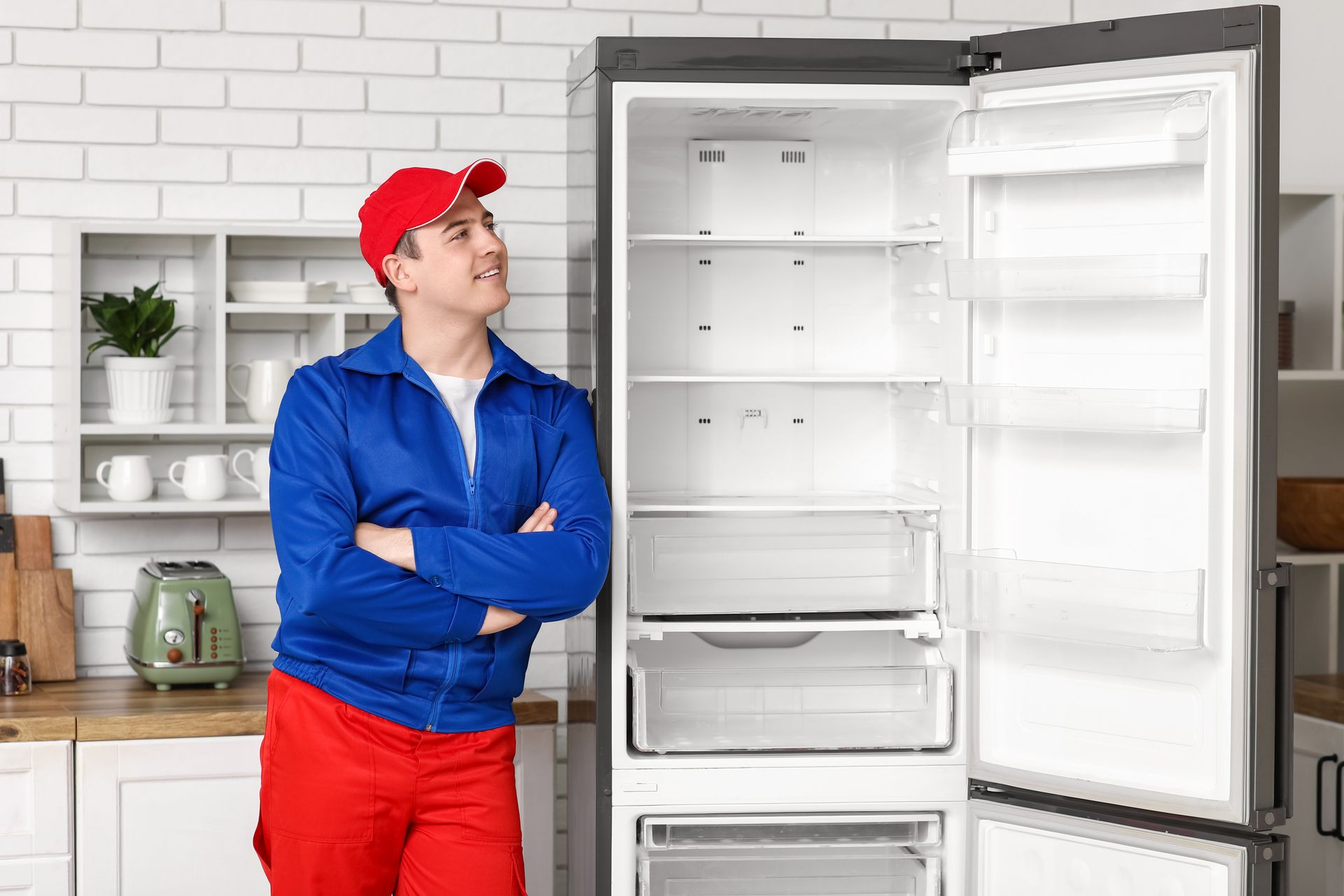 Man in work uniform looking at an empty refrigerator. Kitchen setting.