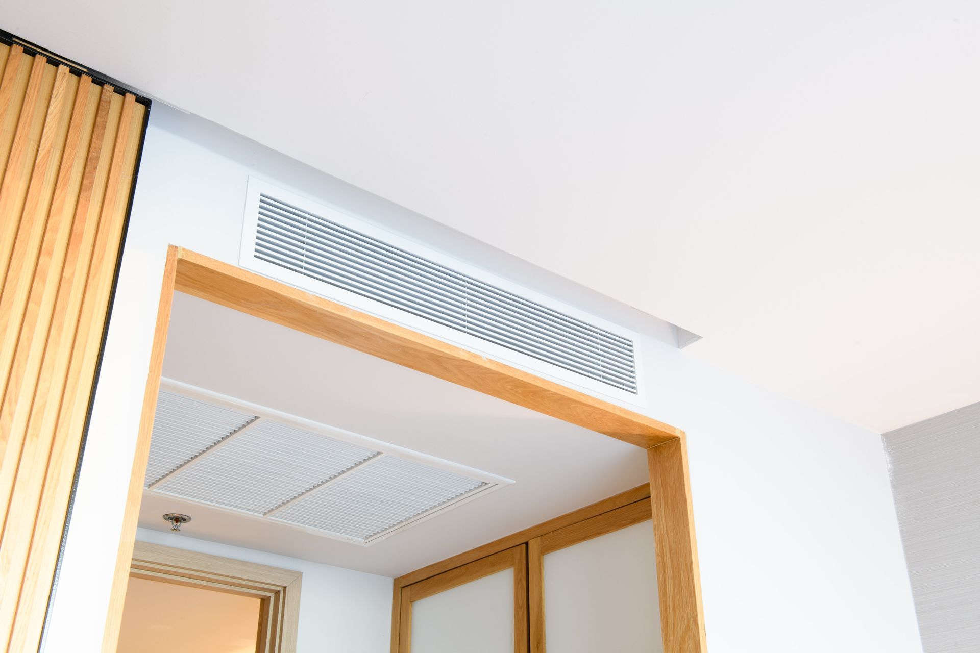 White ceiling with an air vent above a doorway framed in wood.