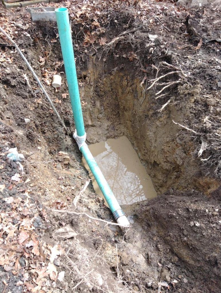 Trench in dirt with a green pipe angled into muddy water.