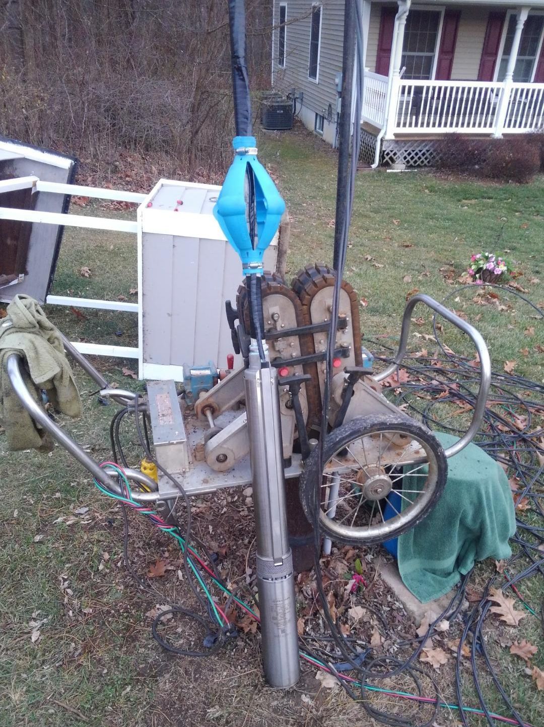Well pump assembly, steel, blue, gray, and green parts, outdoors near a house.