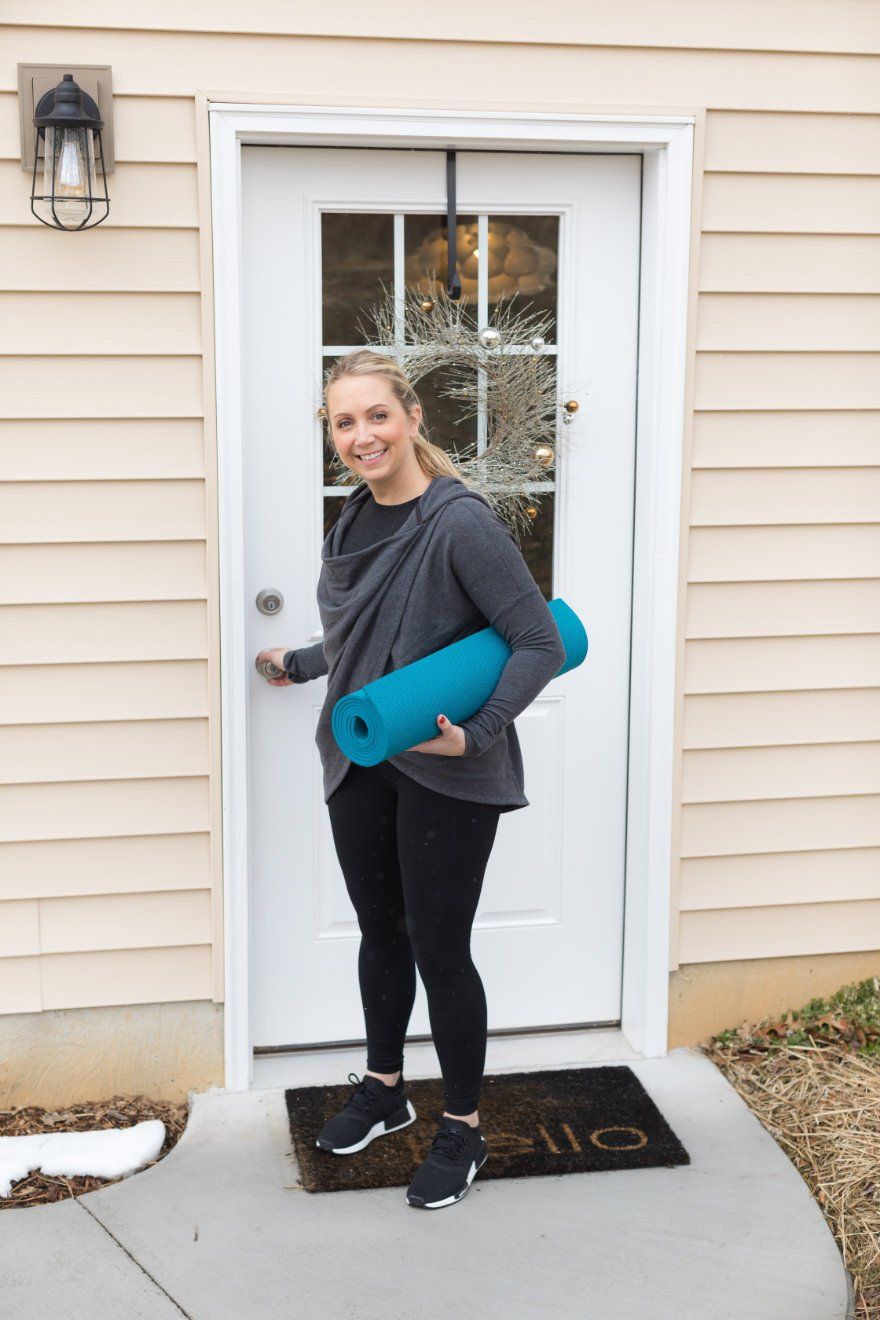 A woman is holding a yoga mat in front of a door.