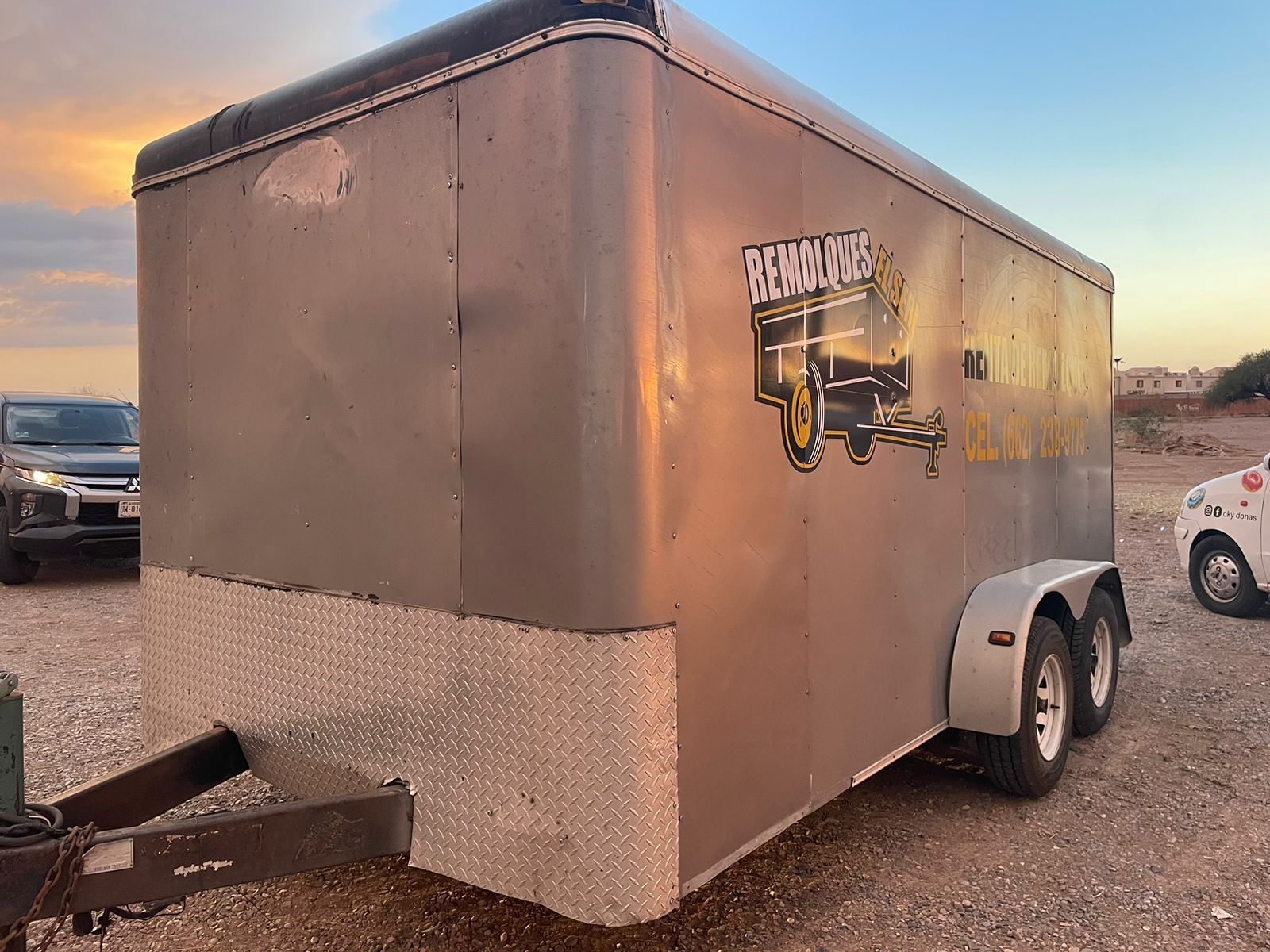 Un remolque con la imagen de un camión está estacionado en un lote de tierra.