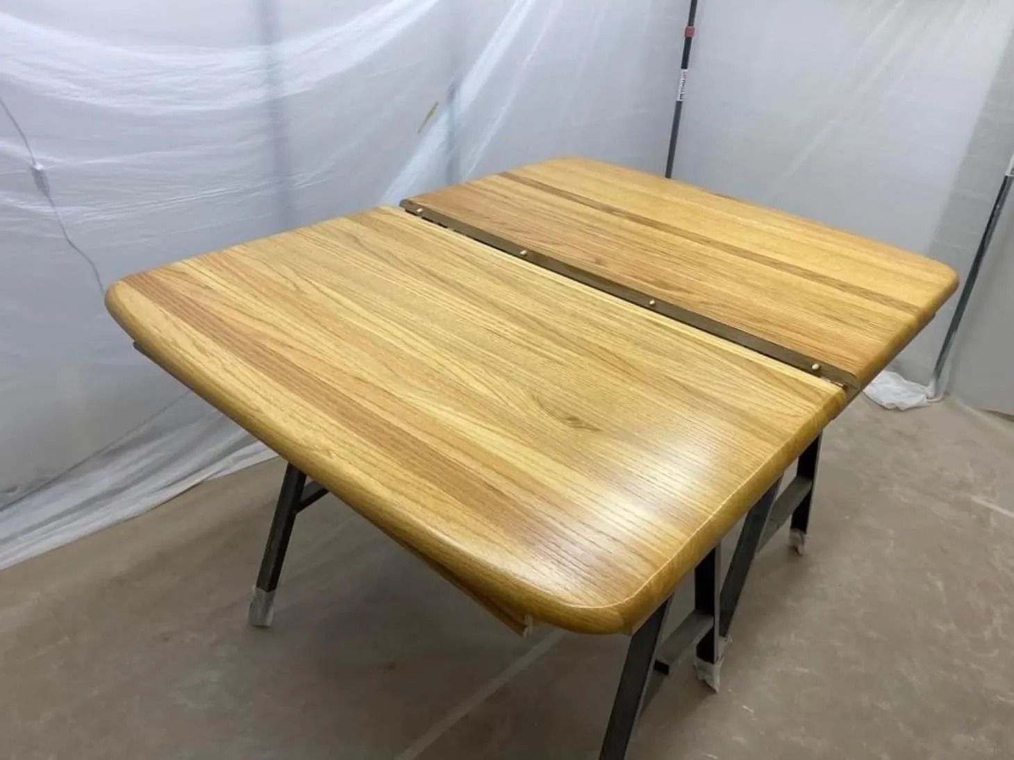 Small wooden folding table with two leaves, shown on metal legs in a plain indoor space