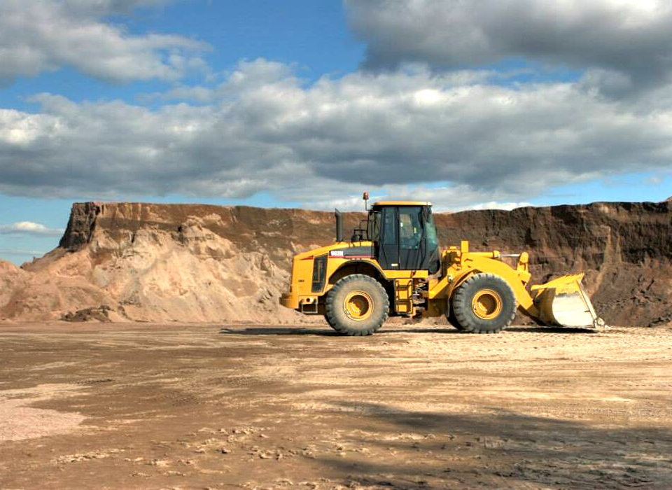 Yellow construction loader on a dirt site with a rocky cliff and cloudy sky