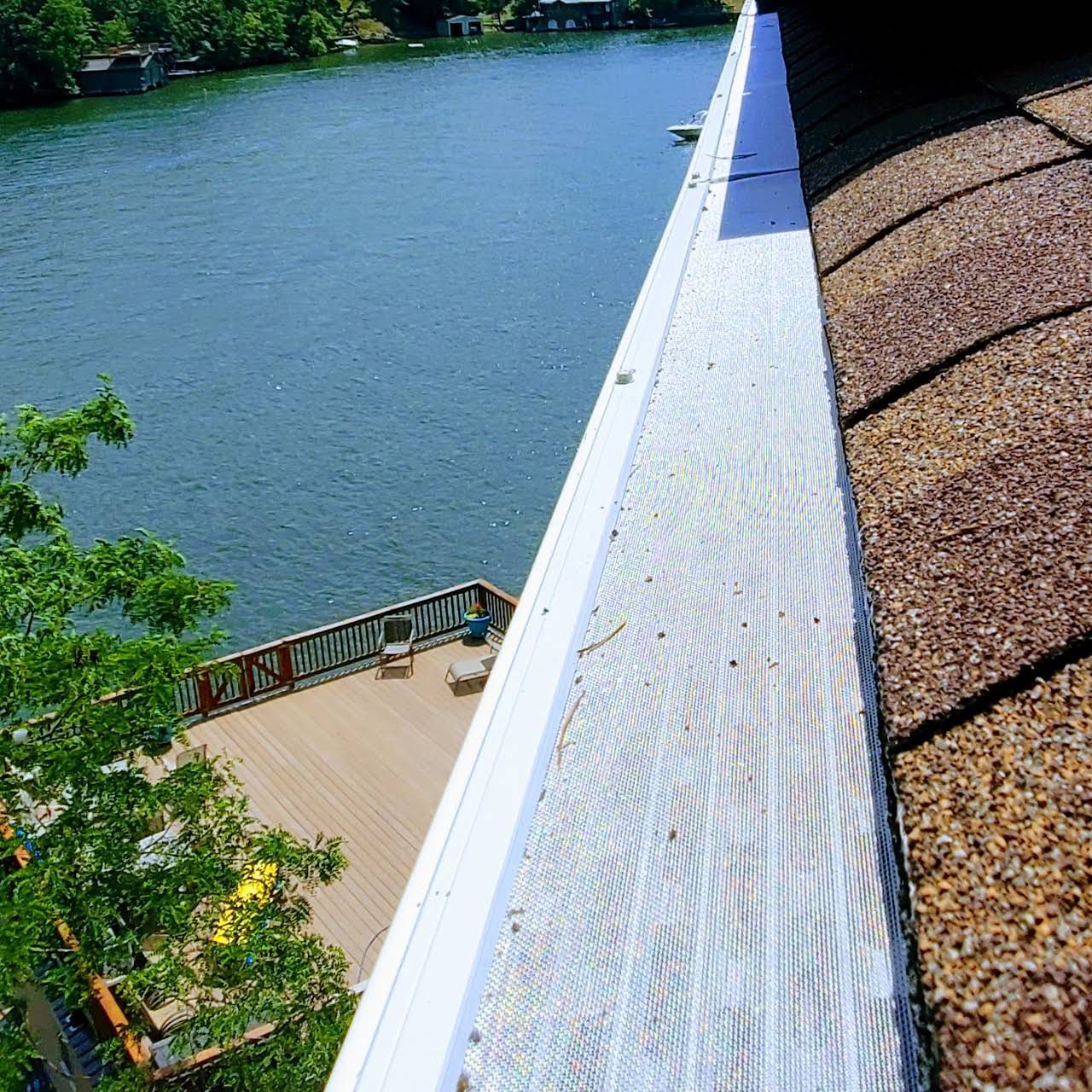 View from a roof gutter, overlooking a lake and wooden deck on a sunny day.
