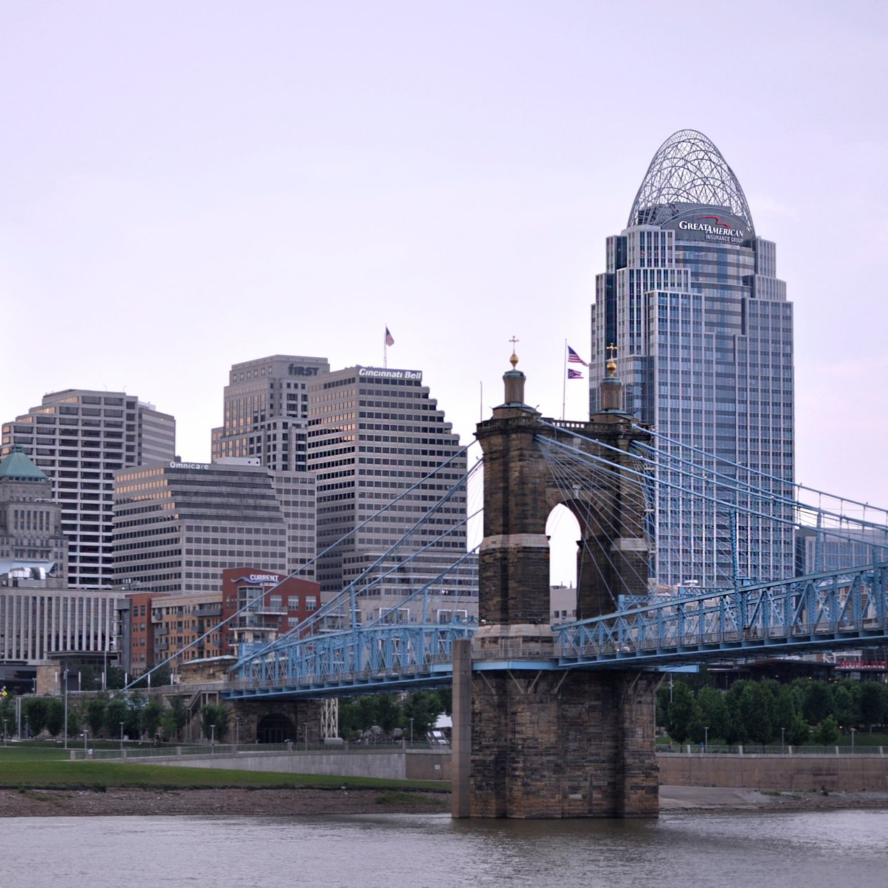 Cincinnati skyline with a blue bridge in the foreground and cloudy sky.