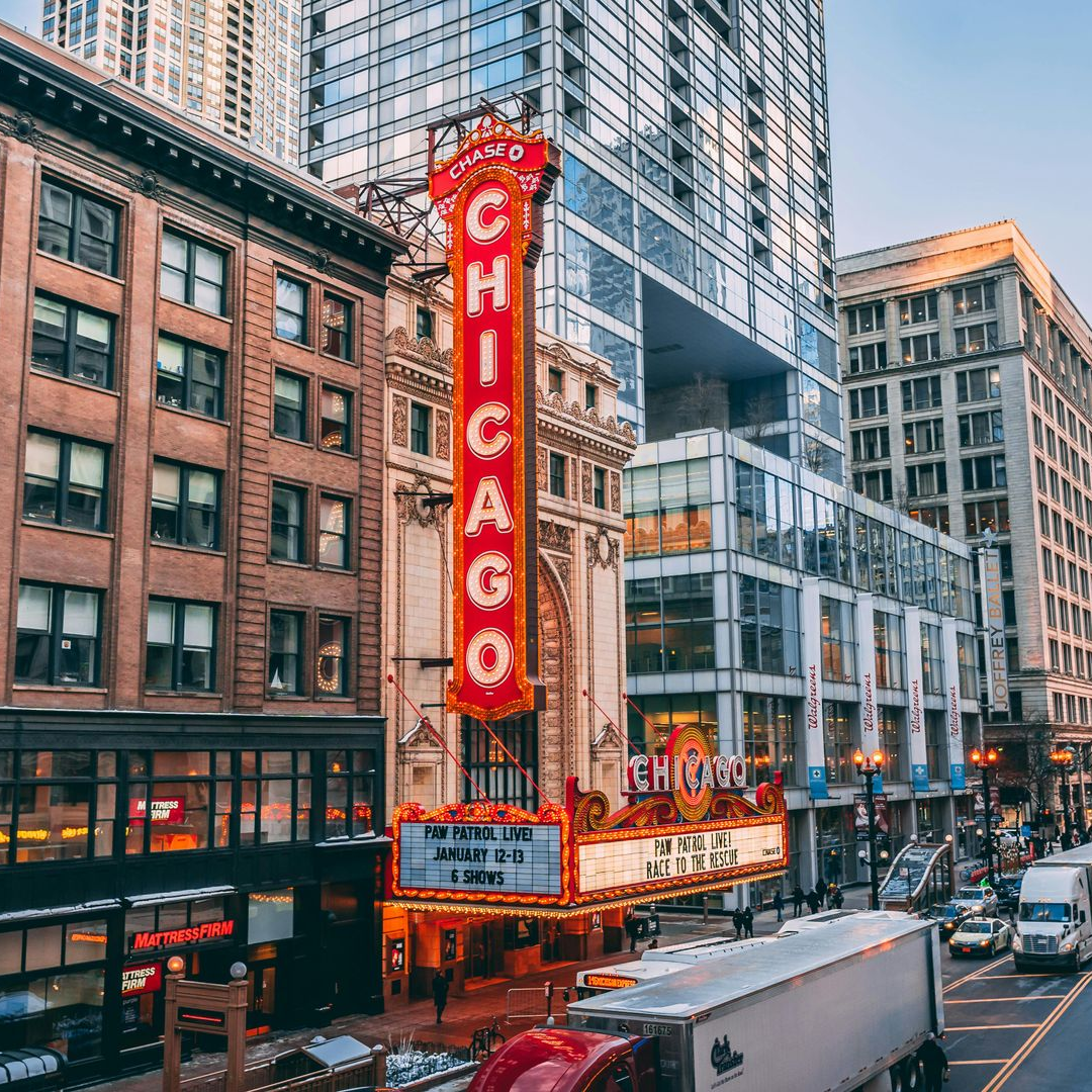 Chicago Theatre with neon sign in city, cars, and tall buildings.