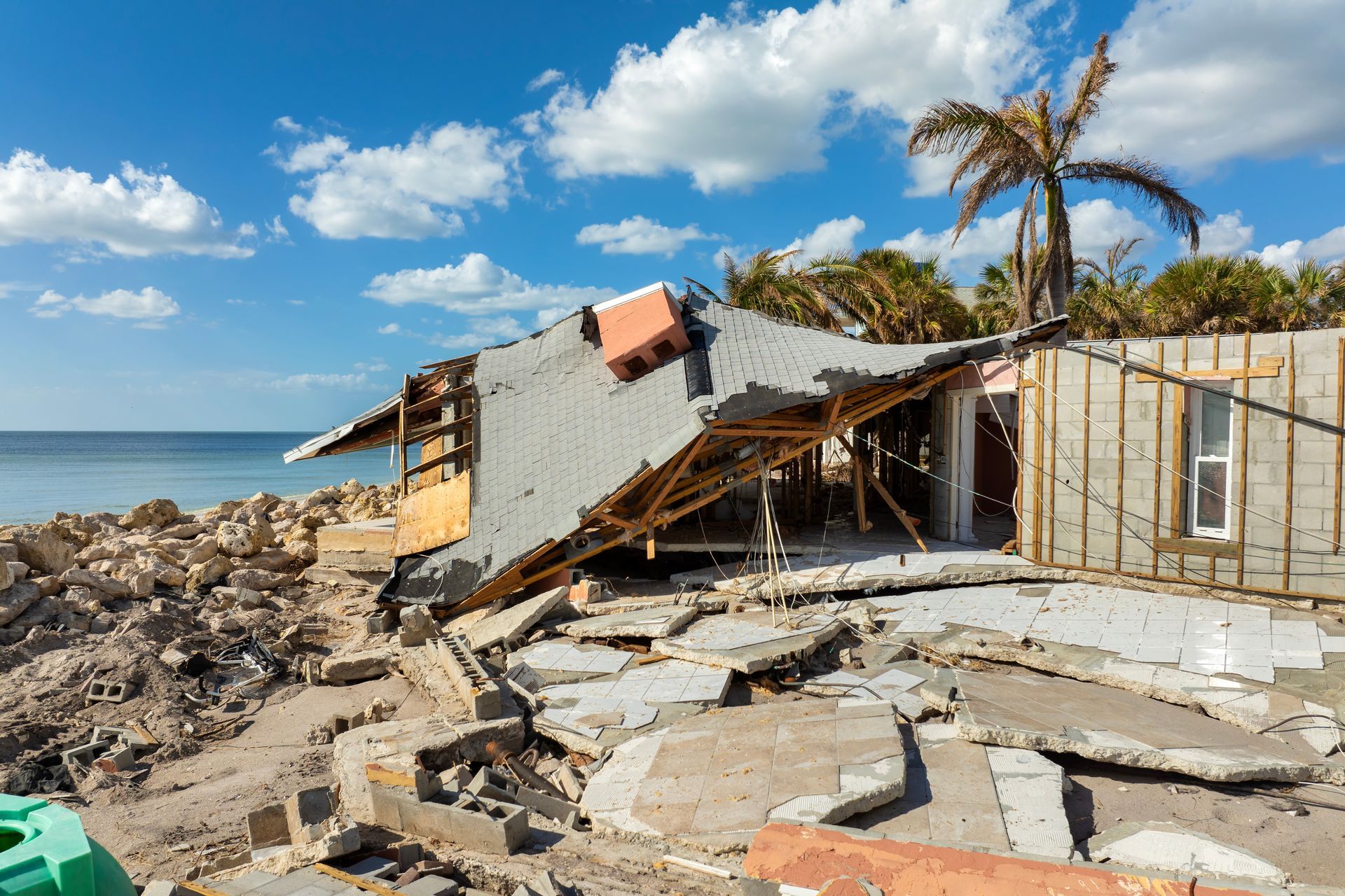 Collapsed beachside building with debris on the shore under a blue sky