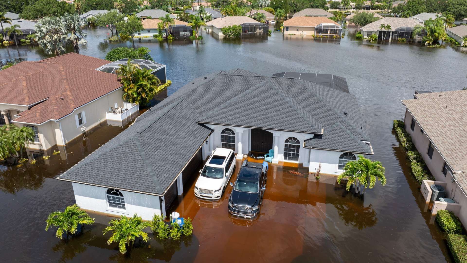 Flooded suburban house with cars parked in high water, viewed from above