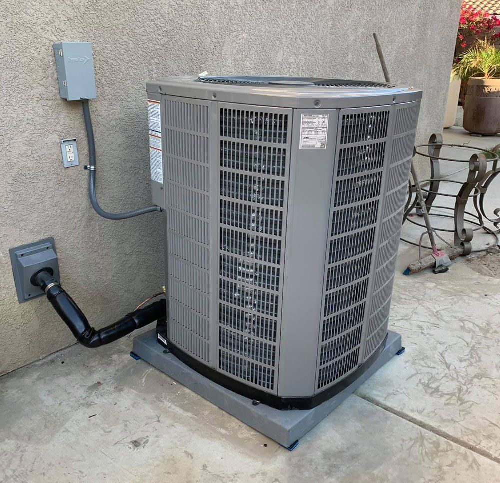 A gray air conditioner is sitting on a concrete floor next to a wall.